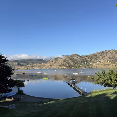 Calm Okanagan lakefront with small boats anchored below golden hills on a clear morning