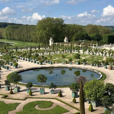 Formal gardens and circular reflecting pool at the Palace of Versailles on a sunny day
