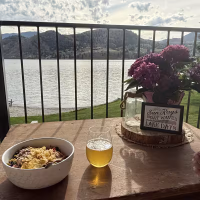 Relaxed lakefront balcony scene with a meal, drink, flowers, and mountain views