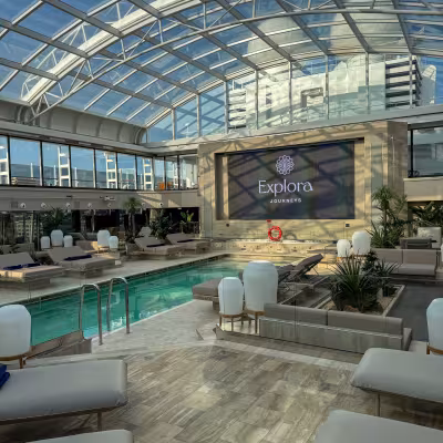 Daytime view of the covered swimming pool and lounge deck aboard Explora Journeys