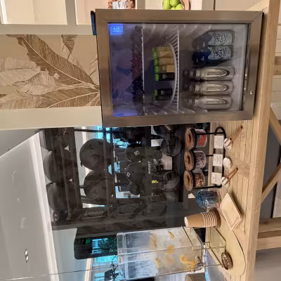 Fitness center refreshment station with infused water, jars of healthy snacks, and a mini fridge stocked with juices, wellness shots, and coconut water next to a glass wall of gym equipment