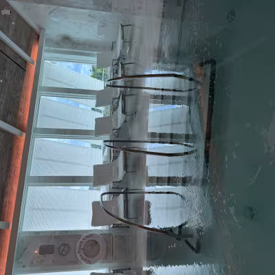 Serene indoor spa pool with bubbling water, metal handrails, and a row of white lounge chairs in front of tall windows letting in soft natural light