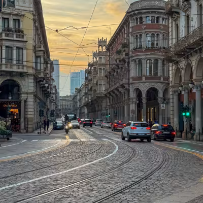 Historic Milan street with tram tracks and ornate buildings at sunset, Italy
