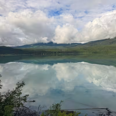Calm alpine lake reflecting clouds and forested mountains along the Alaska Railroad route
