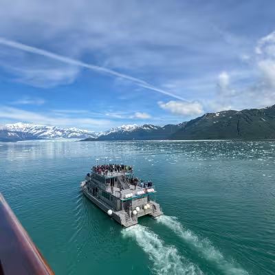 Small tour boat cruising toward Hubbard Glacier with icebergs floating in the water, Alaska