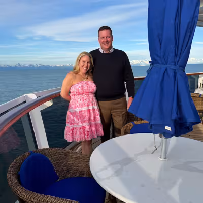Couple posing on the ship's deck with snow-capped Alaska mountains in the background