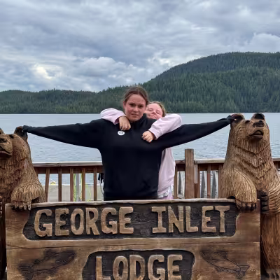 Teens posing between carved bear statues at the George Inlet Lodge sign in Ketchikan, Alaska