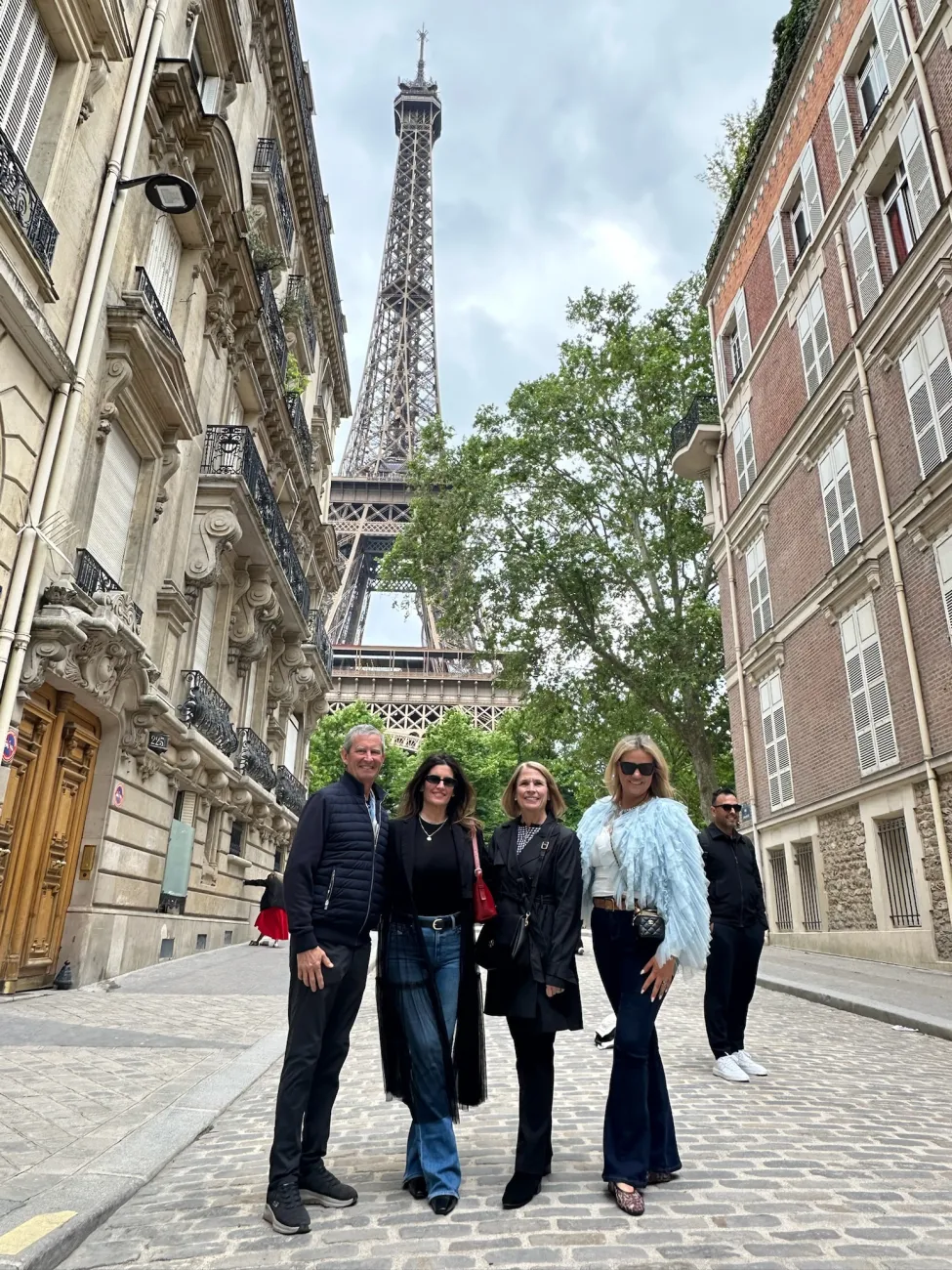 Friends posing on a cobblestone Paris street with the Eiffel Tower rising between Haussmann buildings