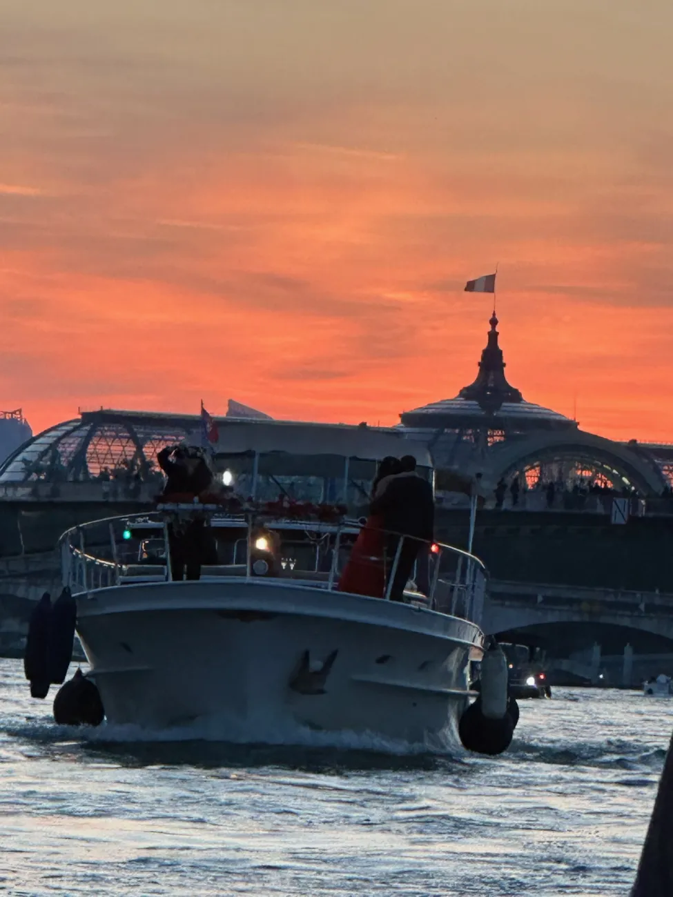 Motorboat cruising the Seine at sunset with Paris landmarks silhouetted against an orange sky