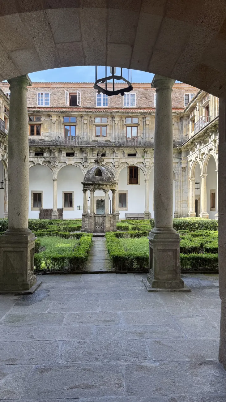 Historic cloister courtyard with stone well and manicured hedges in Santiago de Compostela